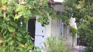 Una casa rústica con terraza de madera, un pequeño jardín y una puerta que da al interior.