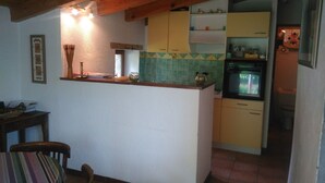 A compact kitchen with a wooden ceiling, a small dining area with a chair, and a tiled backsplash. - renovated cottage quiet and comfortable in South Ardèche in the valley of the Balm (BEAUMONT)