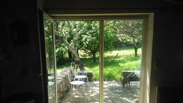A room with a sliding glass door leading to an outdoor patio area with a barbecue grill, chairs, and a dog. - renovated cottage quiet and comfortable in South Ardèche in the valley of the Balm (BEAUMONT)