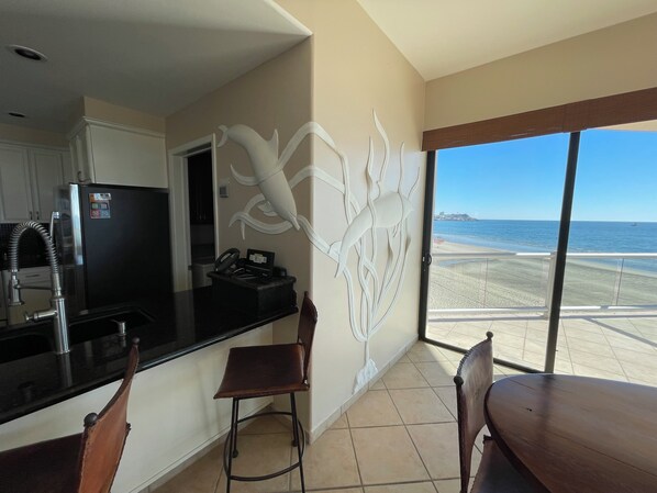 A kitchen with a refrigerator, a coffee machine, and a dining area with a table and chairs.