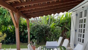 A covered outdoor patio with a stone floor, a glass table, and white plastic chairs.