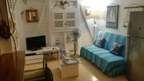 A living room with a TV, a fan, a sofa with cushions, a coffee table, and a refrigerator.