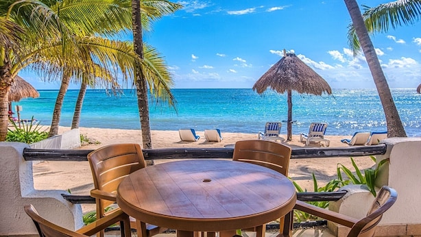 A beachside patio with a round wooden table and chairs, overlooking the ocean. - Ground-Floor Beachfront Living with Private Patio (Akumal)