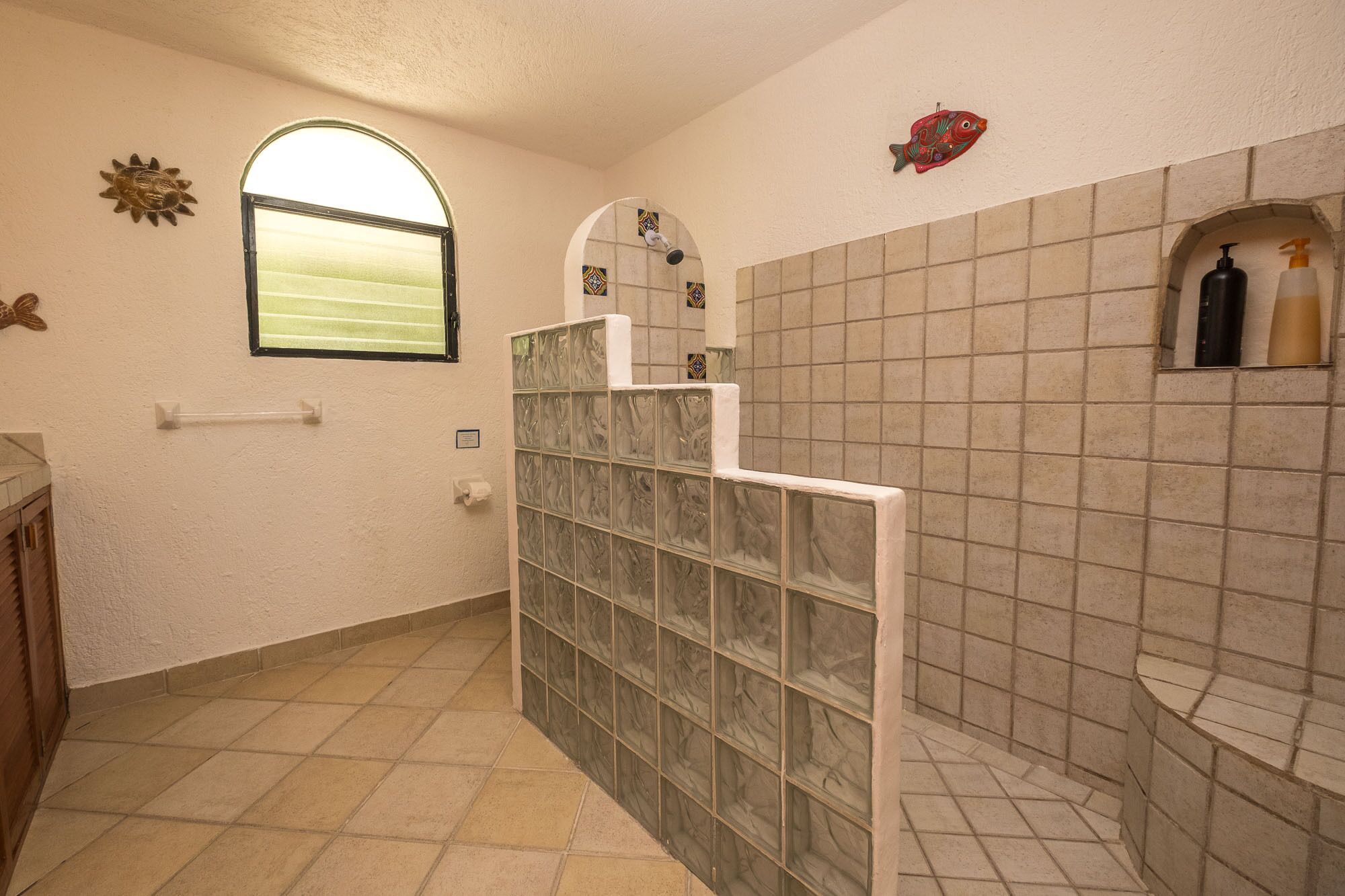 Een badkamer met betegelde vloer, raam, douche en toilet.