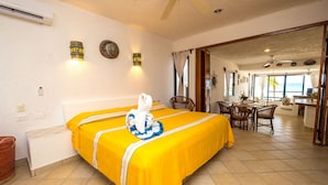 A hotel room with a bed, a dining area, and a view of the ocean. - Ground-Floor Beachfront Living with Private Patio (Akumal)