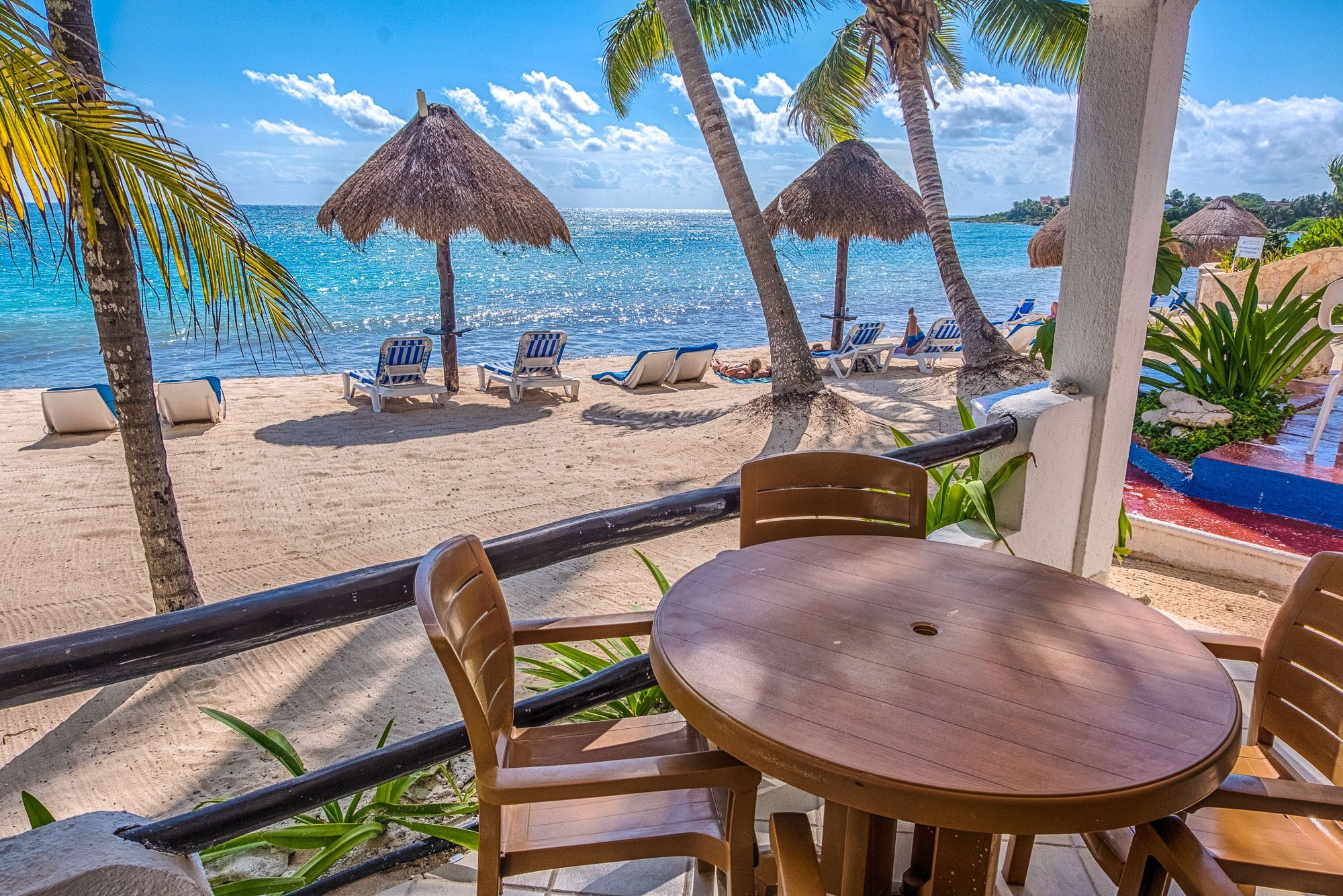 A beachside seating area with a table and chairs, a thatched umbrella, and a view of the ocean.
