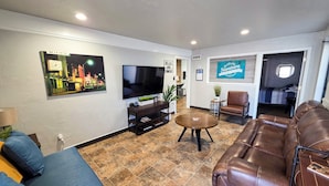 A living room with a sofa, a brown leather couch, a TV, a coffee table, and a wall with a cityscape picture.