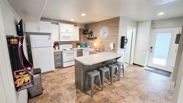 A modern kitchen with white cabinets, a central island with stools, a refrigerator, and a stove.