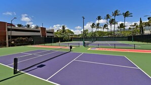 Un campo da tennis con più campi, una rete e palme circostanti.