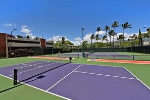 Un campo da tennis con più campi, una rete e palme circostanti.