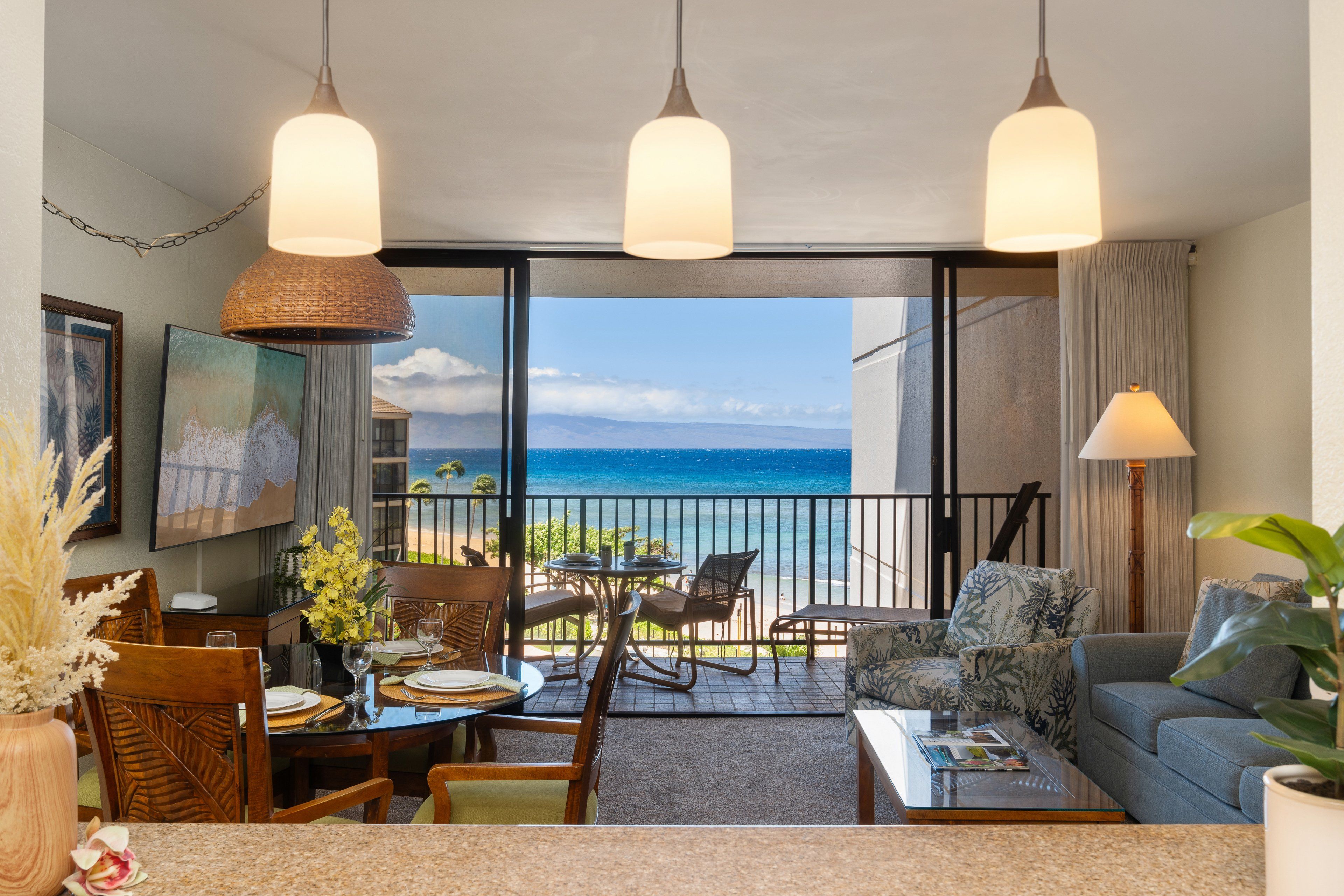 A room with a dining area, a sofa, and a balcony with a view of the ocean.