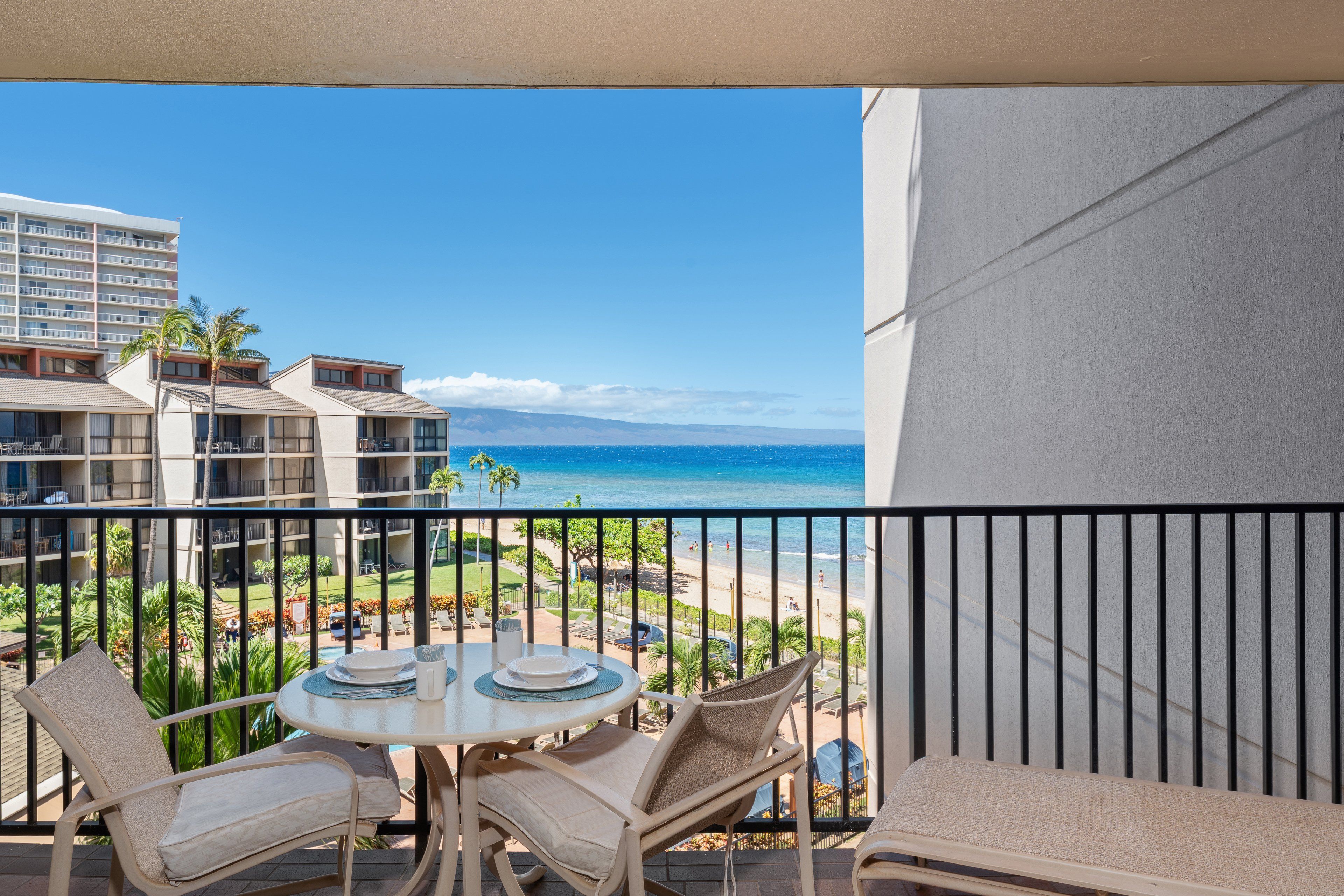 Un balcon avec une table et des chaises, donnant sur une plage et sur les bâtiments d’un hôtel.