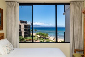 A hotel room with a large window overlooking a beach and ocean.