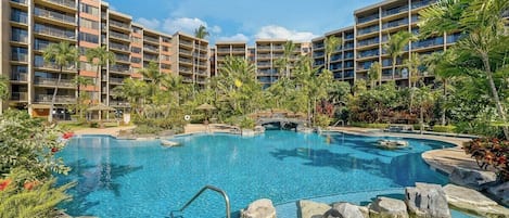 Ein Hotel mit mehreren Balkonen, einem Pool inmitten von Felsen und tropischer Bepflanzung.