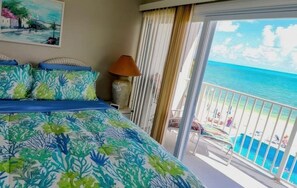A hotel room with a bed, a nightstand, a lamp, and a balcony with a view of the ocean. - Paradise Found – Oceanfront Condo w/ Pool Views & Private Beach in Key Colony! (Key Colony Beach)