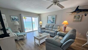 A living room with a ceiling fan, two sofas, a coffee table, and a view of the ocean through large windows. - Paradise Found – Oceanfront Condo w/ Pool Views & Private Beach in Key Colony! (Key Colony Beach)