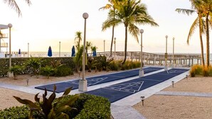 A boardwalk with shuffleboard courts, palm trees, and a beach view. - Paradise Found – Oceanfront Condo w/ Pool Views & Private Beach in Key Colony! (Key Colony Beach)