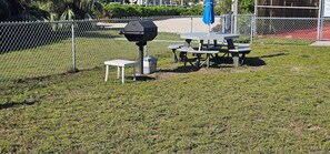 A picnic table with a grill, a small table, and a trash can in a grassy area. - Paradise Found – Oceanfront Condo w/ Pool Views & Private Beach in Key Colony! (Key Colony Beach)