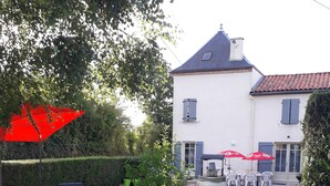 Een wit huis met een pannendak, een houten omheining en tuinmeubilair onder rode parasols.
