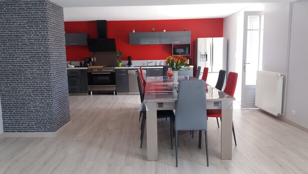 Een moderne keuken met rode wanden, een inbouwoven en een eethoek met een glazen tafel en stoelen.