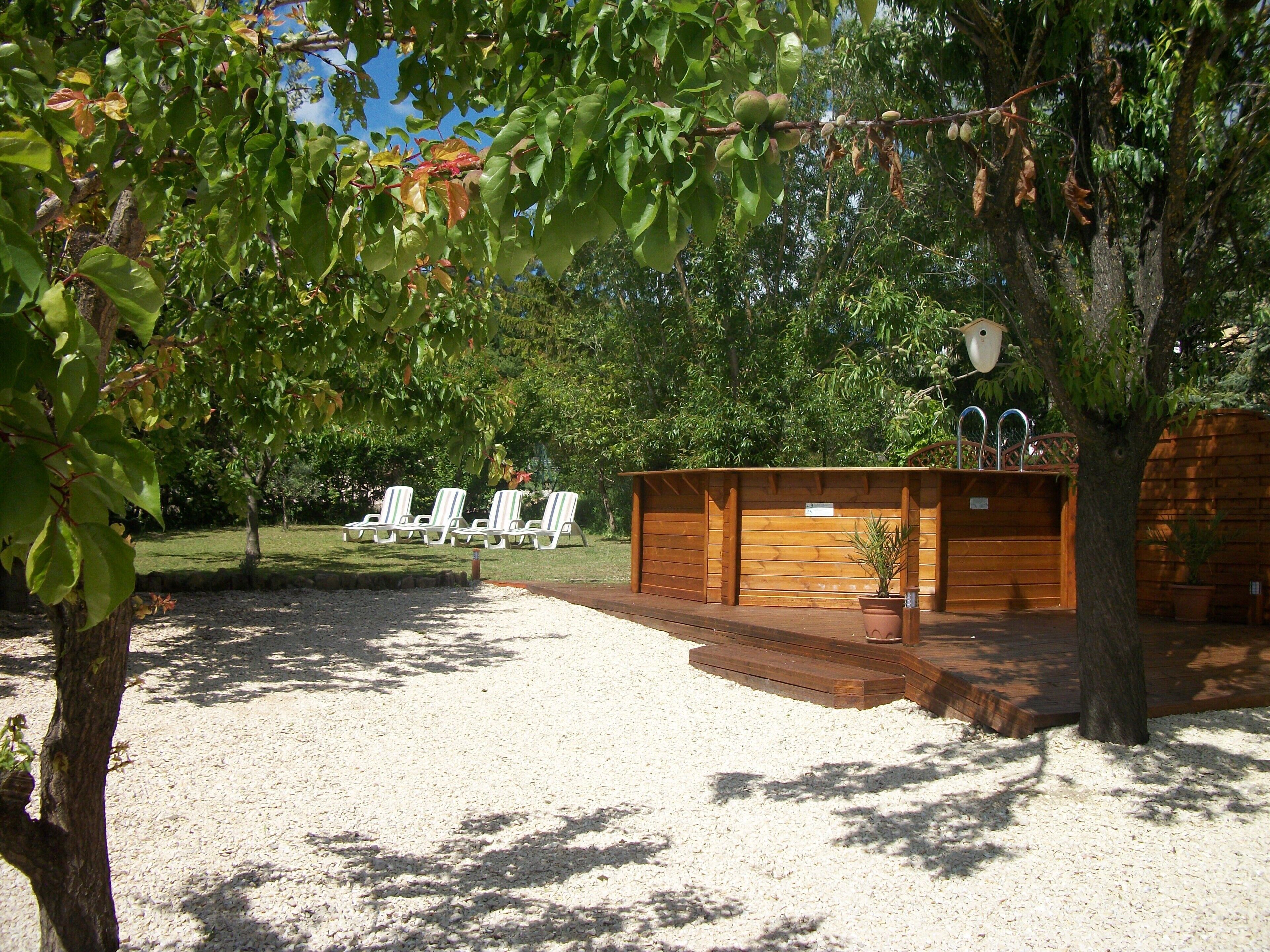 Un espace extérieur abrité, avec des chaises blanches, une structure en bois dotée d’un toit et un sol recouvert de gravier.