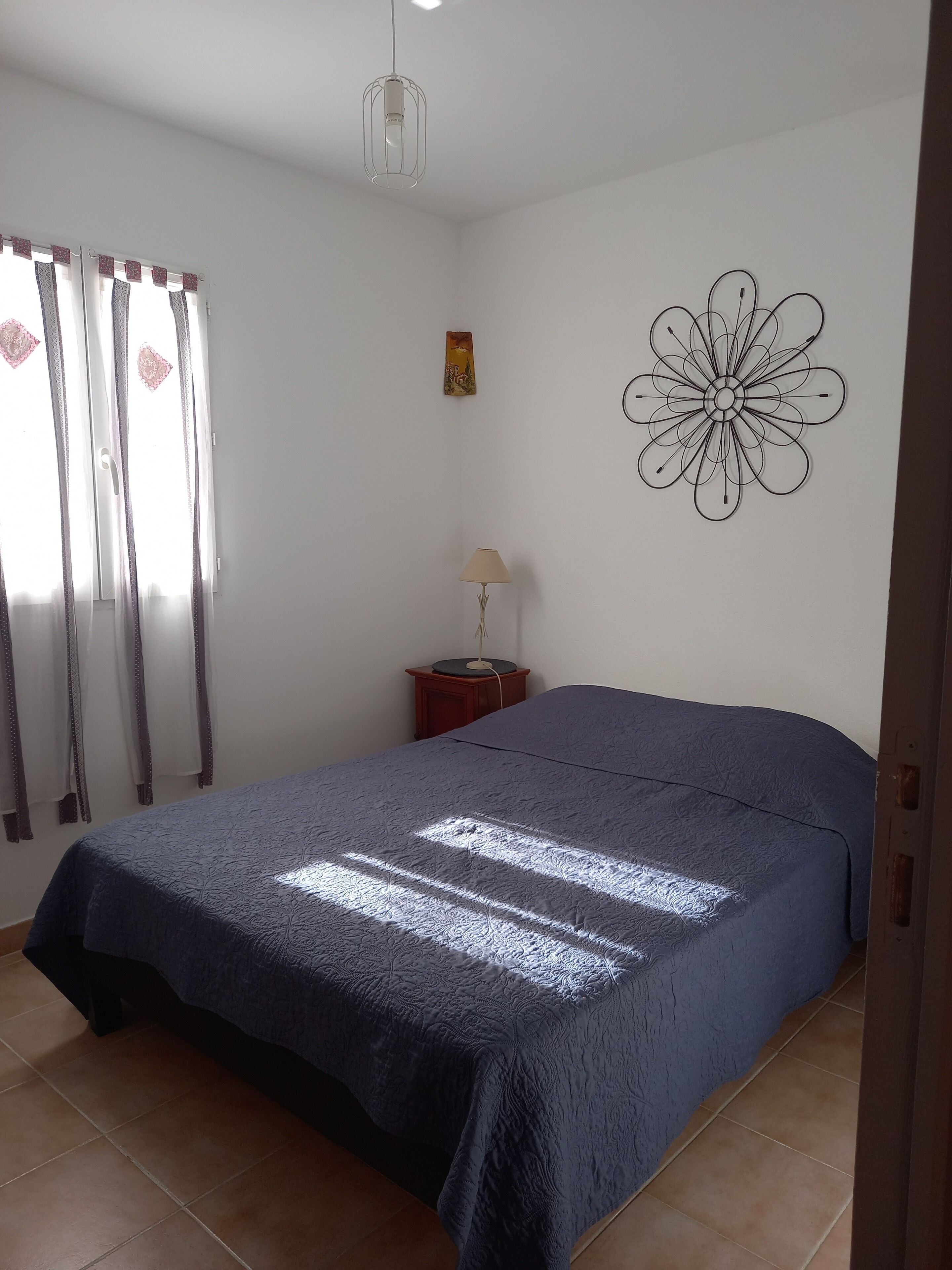 Ein Schlafzimmer mit einem Bett, einer Lampe, einem Wandbild und Vorhängen.