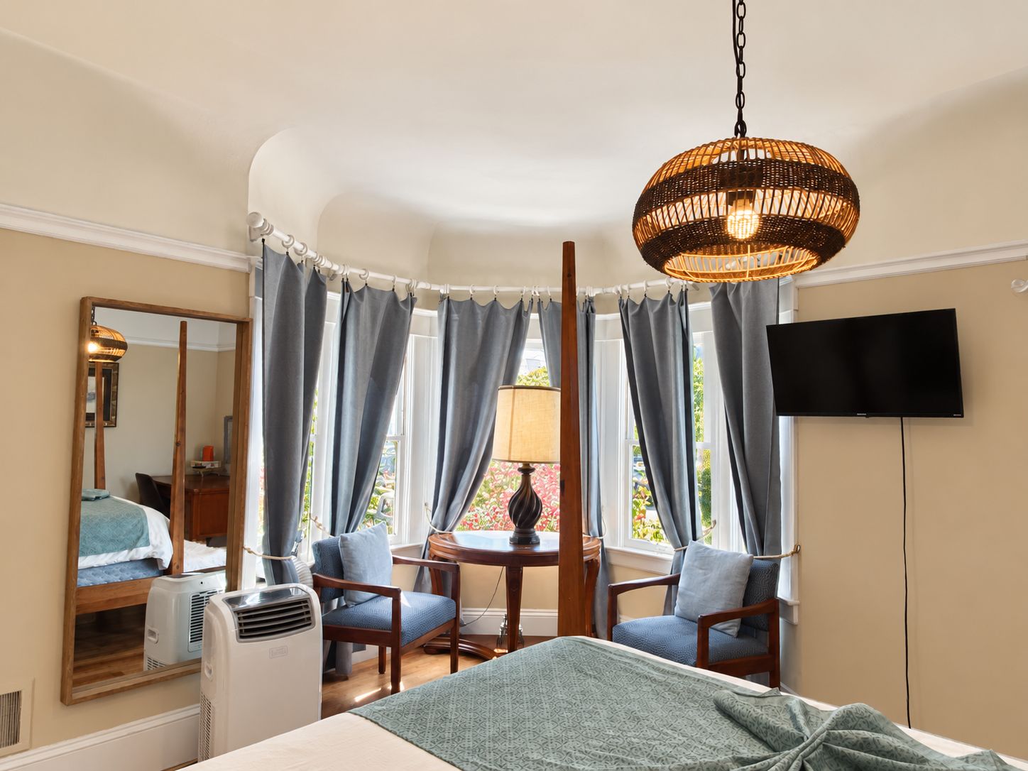 Ein Hotelzimmer mit einem Bett, zwei Stühlen, einem Tisch, einem Spiegel, einem Fernseher und einer Deckenleuchte.