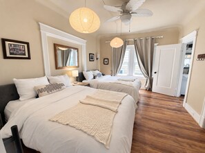 A hotel room with two beds, a ceiling fan, a large window with curtains, and a wooden floor. - Historic 4BR Alameda Victorian Near Beach & SF (Alameda)