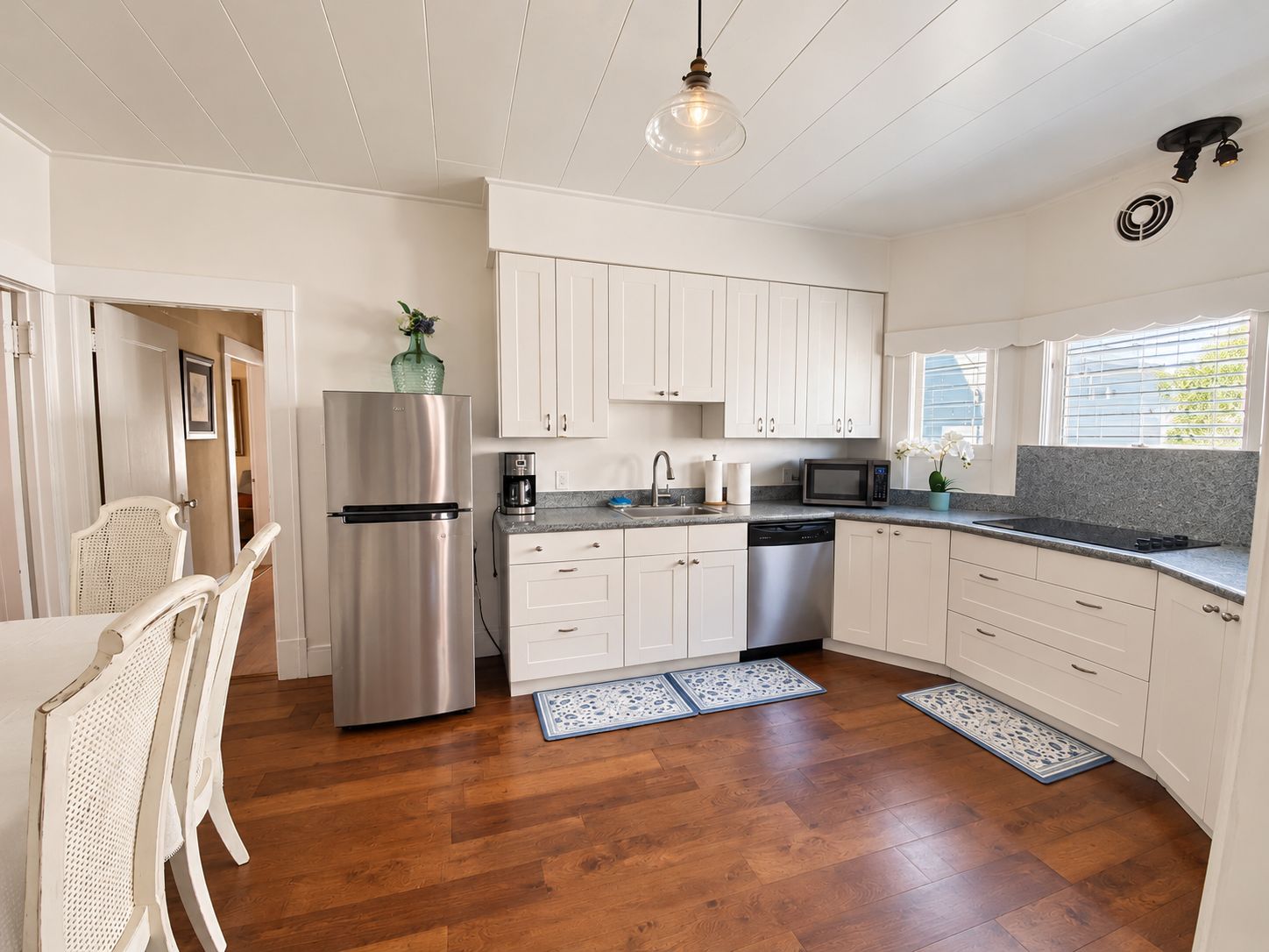 A modern kitchen with white cabinets, stainless steel appliances, and a wooden floor.