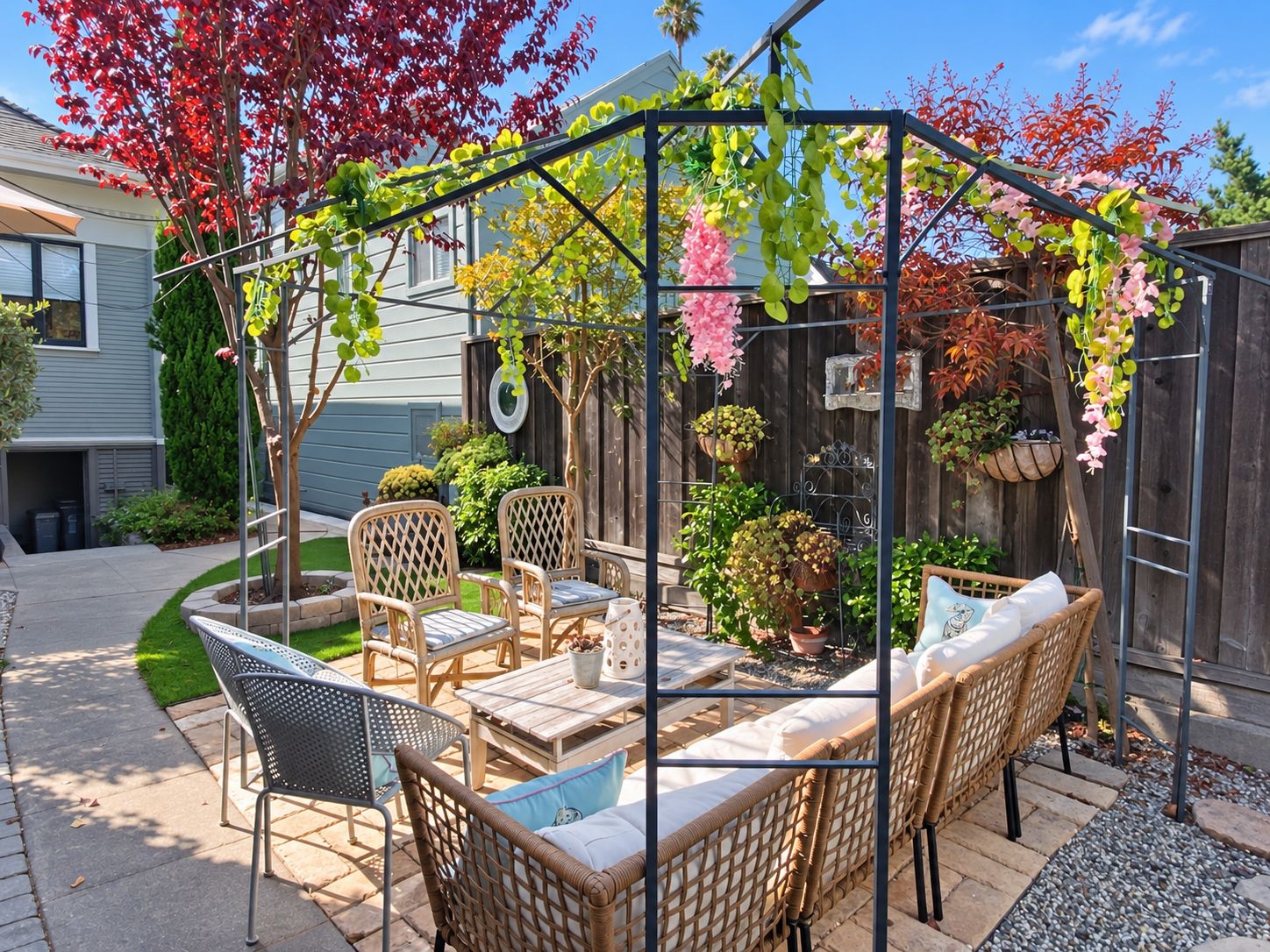 Un patio couvert aménagé avec des meubles en osier, une pergola ornée de plantes suspendues et, au fond, une clôture en bois.
