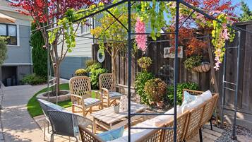 Un patio couvert aménagé avec des meubles en osier, une pergola ornée de plantes suspendues et, au fond, une clôture en bois.