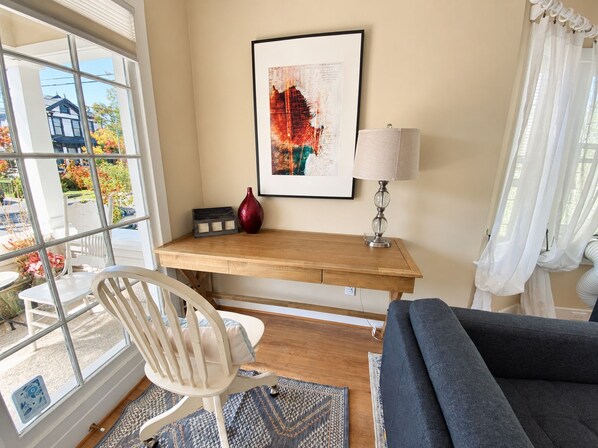 Una habitación con un escritorio de madera, una silla, un sofá, una lámpara y un cuadro en la pared.