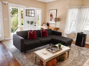 A living room with a sectional sofa, a coffee table, a rug, a door with a window, and a lamp. - Historic 4BR Alameda Victorian Near Beach & SF (Alameda)