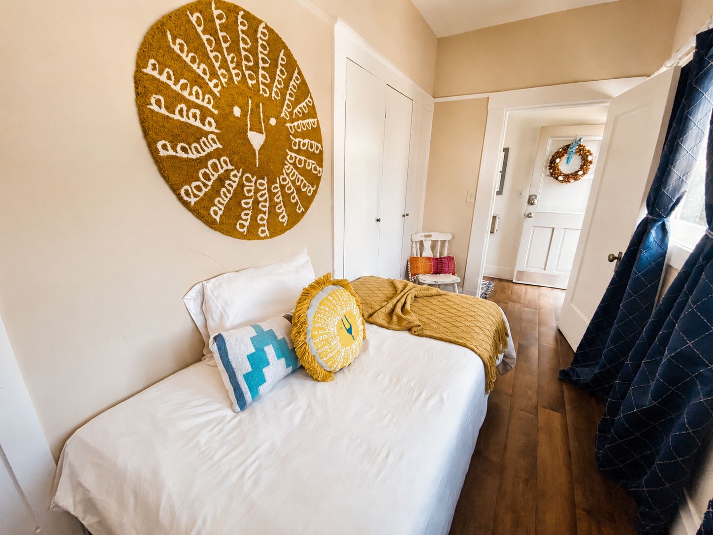 A bedroom with a bed, pillows, a wall clock, a door, and a curtain.