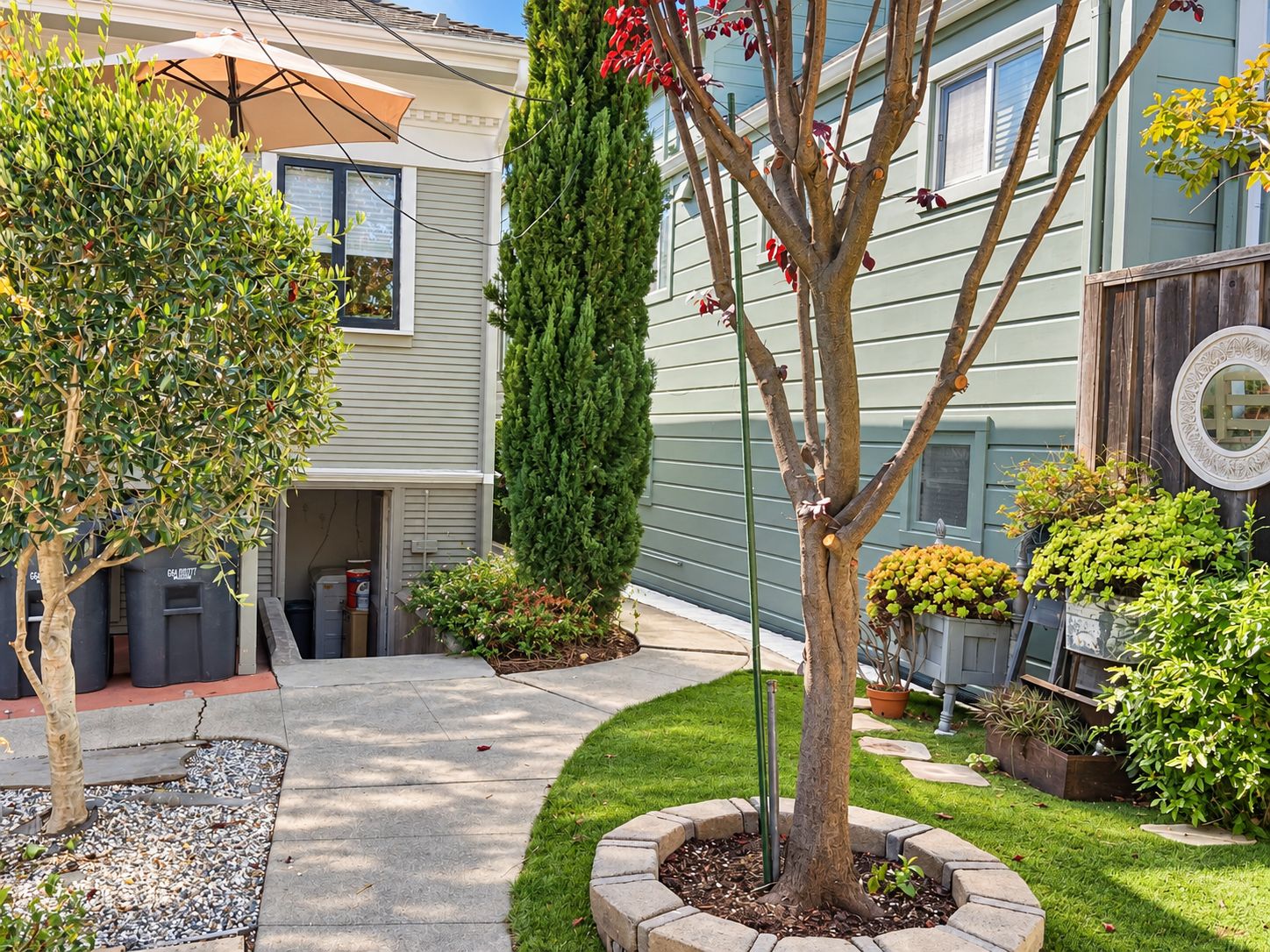 A residential property with a paved driveway, a well-maintained lawn, and various potted plants.