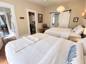 Un dormitorio con dos camas, un vestidor, una silla y una mesita de noche.