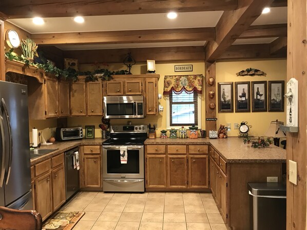 A kitchen with wooden cabinets, stainless steel appliances, and a window with a floral curtain.