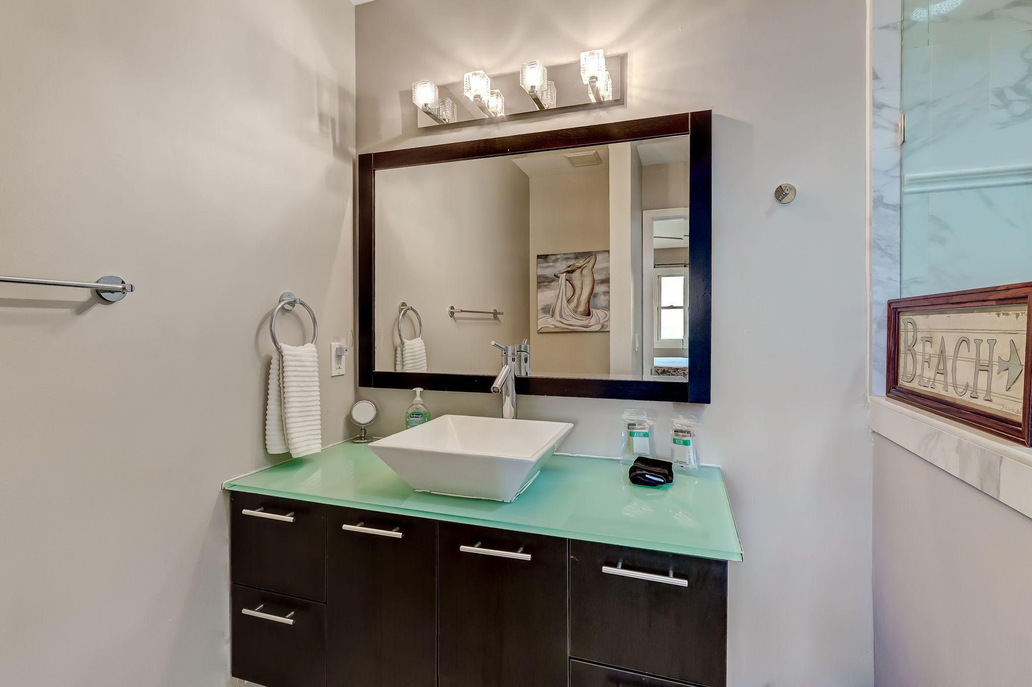 A bathroom with a large mirror, a white sink, and a green countertop.
