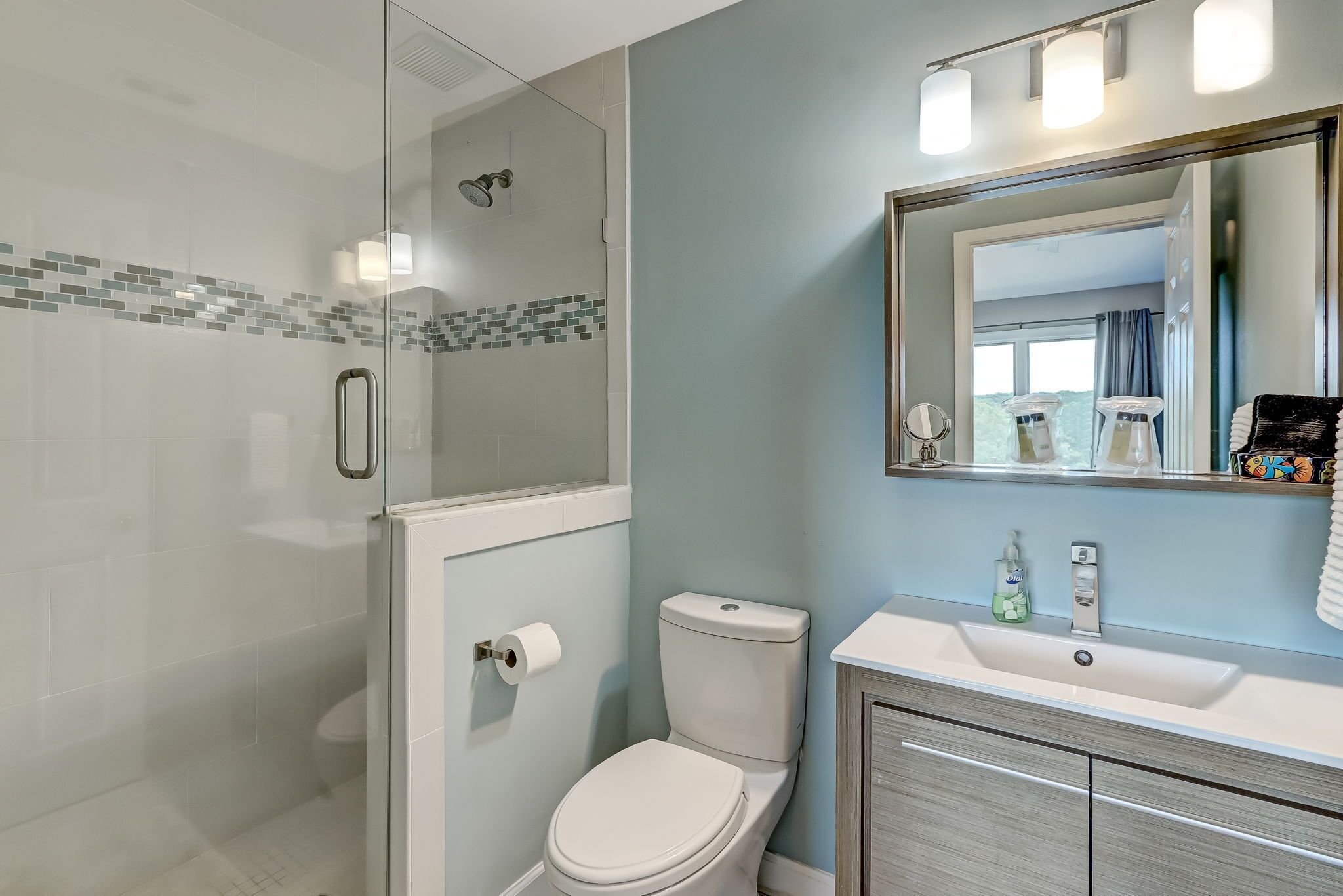 A bathroom with a glass-enclosed shower, a white toilet, and a sink with a mirror above it.