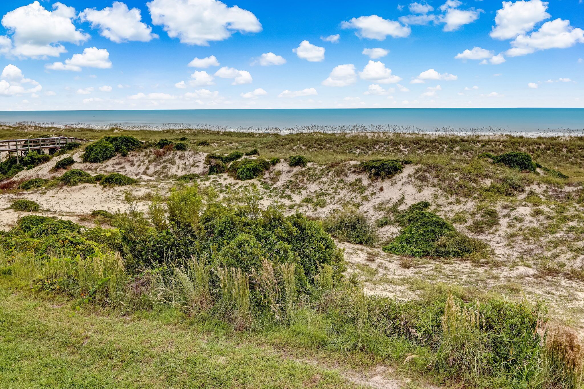 Eine Küstenlandschaft mit Dünen, einer Holzbrücke und blauem Himmel.