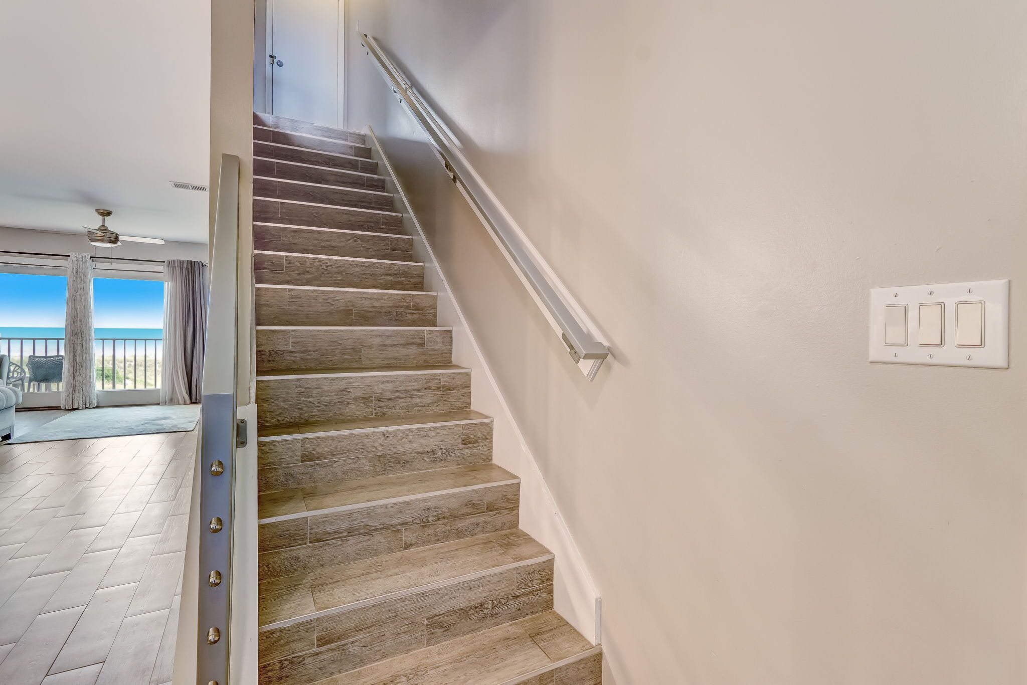 Un escalier avec des marches en bois et une rampe métallique, menant à une pièce dotée d’une grande fenêtre et offrant une vue sur l’extérieur.
