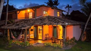 A two-story house with a covered patio, open windows, and a visible kitchen area. - Charm Bahia Residências (Porto Seguro)