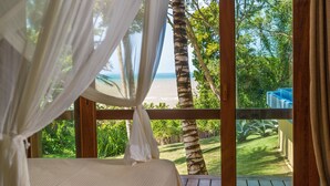 A bedroom with a view of the beach, a wooden deck, and a garden. - Charm Bahia Residências (Porto Seguro)