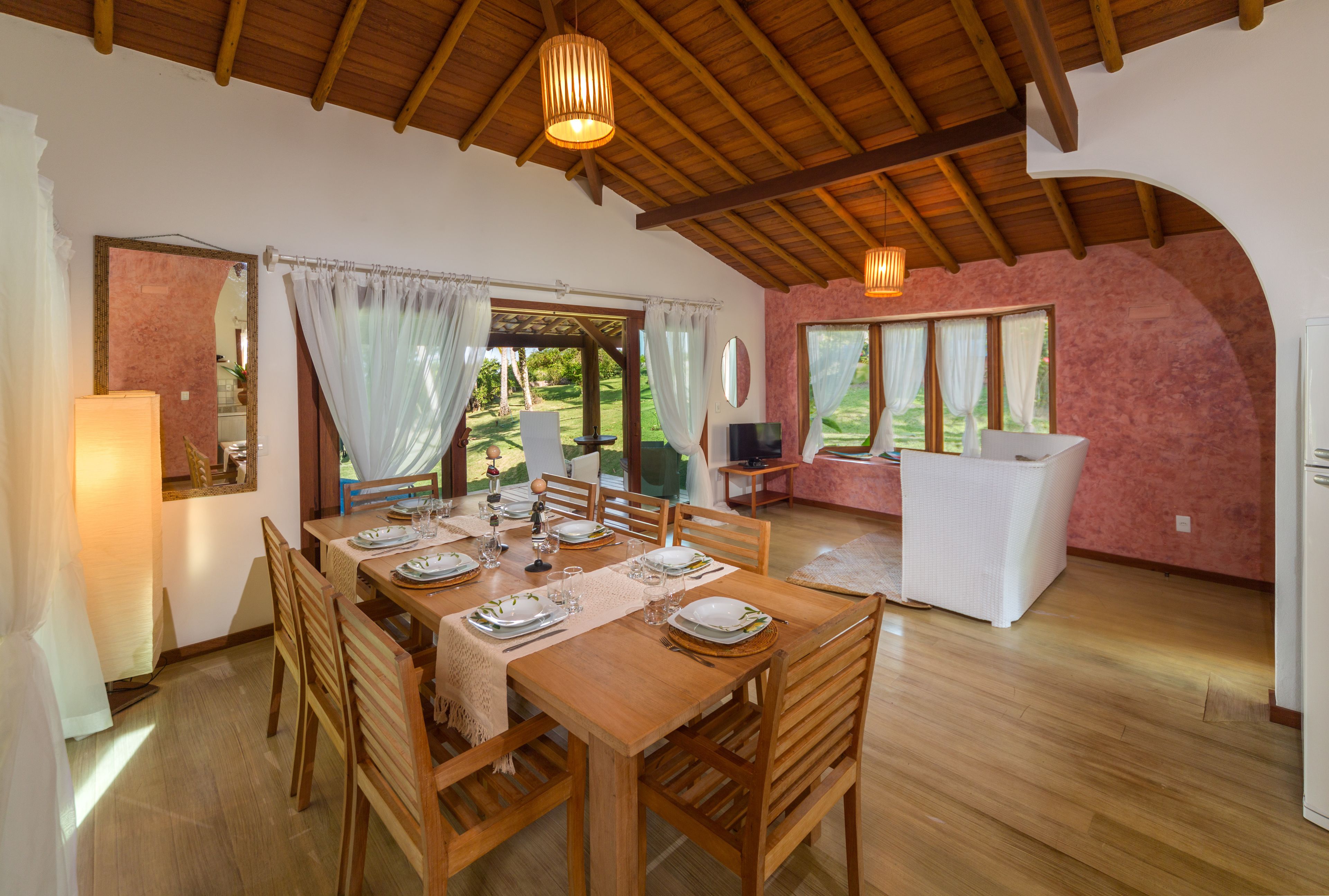 A dining area with a wooden table set for four, surrounded by wooden chairs. There is a kitchen area with a white countertop and a sink visible in the background.