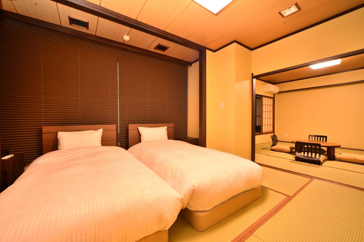 A hotel room with two beds, a wooden headboard, a large mirror, and a traditional Japanese tatami mat floor.