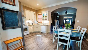 Una cocina con armarios blancos, piso de madera y un comedor con mesa azul y sillas blancas.