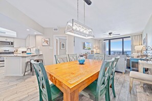 A modern kitchen with a central island, dining area with a wooden table, and a balcony with a view.
