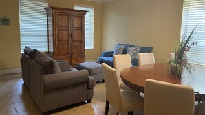 Un salon avec un canapé marron, un divan bleu, un meuble en bois et une table à manger avec des chaises.