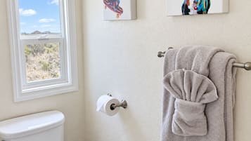 Een badkamer met een toilet, een raam met uitzicht op de omgeving en twee kunstwerken in lijsten aan de muur.