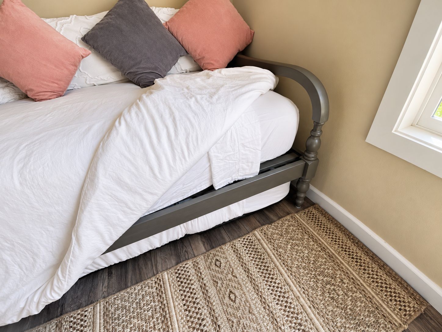 Un lit avec une tête de lit, du linge de lit blanc et un tapis tissé sur un plancher en bois.